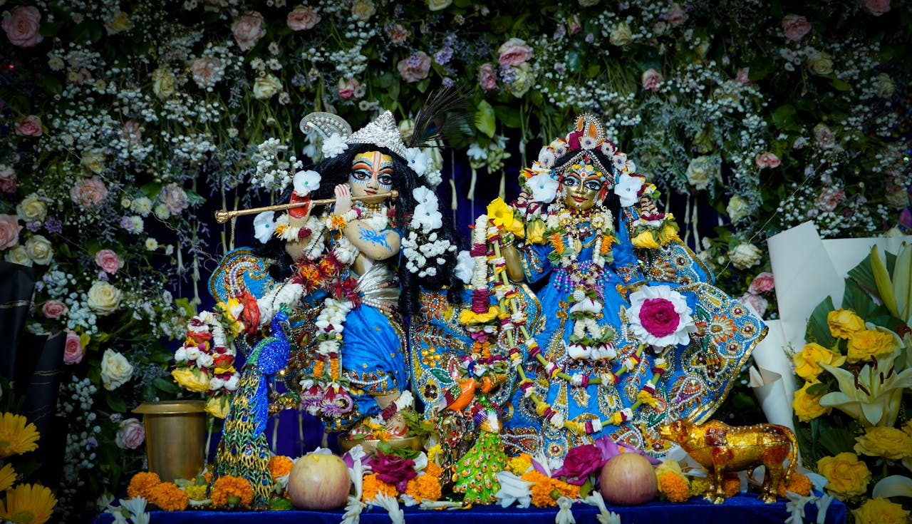 Intricate Krishna and Radha statues adorned with flowers and ornaments, set in vibrant decor.